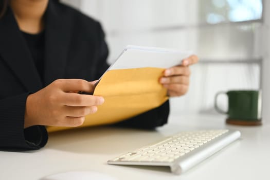 Close up of businesswoman opening confidential envelope at work desk.