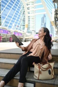 Delighted senior businesswoman using digital tablet in modern city.