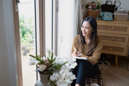 Beautiful young woman writing in notebook while looking out the window.