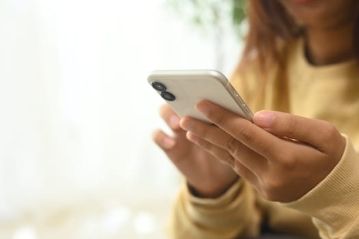 Close up of woman in yellow sweater typing message on her smartphone.