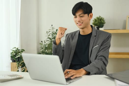 Young entrepreneur celebrating success in online project at work desk.