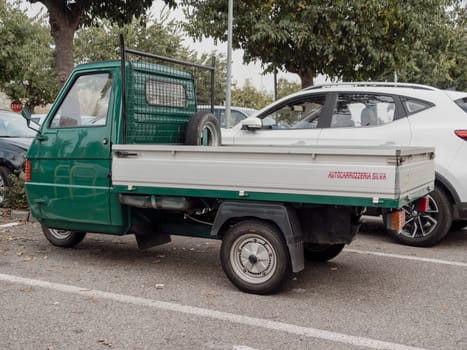 Arquato, PC, italy - October 31st 2024 Small green commercial vehicle Ape piaggio porter parked in an outdoor parking lot, showing its rear part with spare wheel and license plate