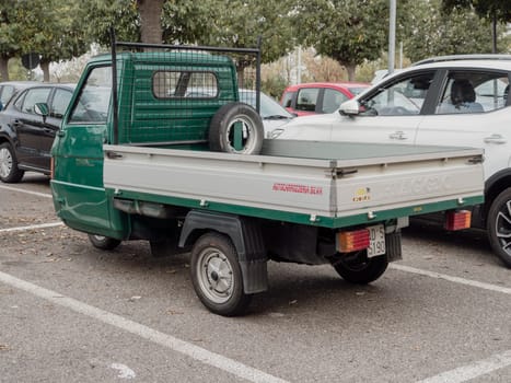 Arquato, PC, italy - October 31st 2024 Small green commercial vehicle Ape piaggio porter parked in an outdoor parking lot, showing its rear part with spare wheel and license plate