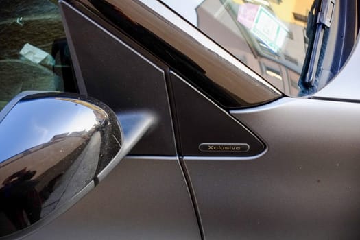 Cremona, Lombardy, Italy - November 7th 2024 Close-up of an xclusive badge on a gray car's door, with the rearview mirror reflecting a street view