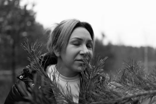 The woman closes her eyes and takes a deep breath, savoring the fresh scent of pine branches while surrounded by tall trees under a muted sky.