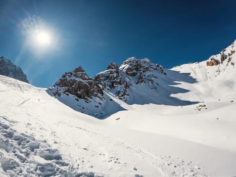 Three picturesque rocky peaks cast shadows from the bright winter sun on a snow-capped high mountain pass.