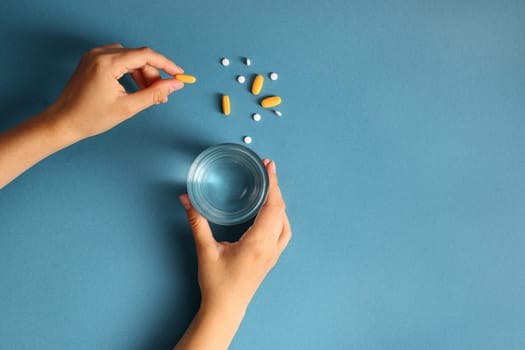Hands holding pills and a glass of water on a blue background. Ideal for medical and healthcare topics.