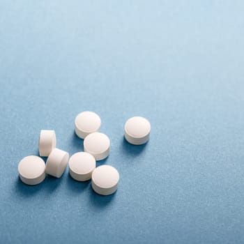 Handful of white medicinal tablets on blue background.