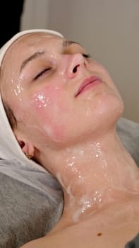 professional cosmetologist applies a white mask on the face of a female client with a brush, close-up