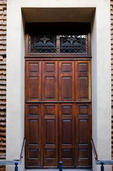 Cremona, Lombardy, Italy - November 7th 2024 Classic wooden door with decorative iron grate, set against a brick wall, showcasing timeless architectural design