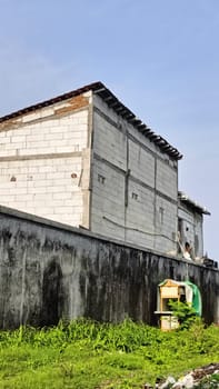 An industrial building partially hidden by a brick wall under a blue sky. The image captures urban architecture with a mix of materials and textures in a relaxed setting.