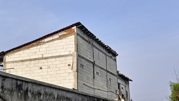 An industrial building partially hidden by a brick wall under a blue sky. The image captures urban architecture with a mix of materials and textures in a relaxed setting.