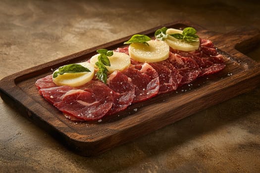 Fresh raw beef slices on a plate set on a dark wooden table..