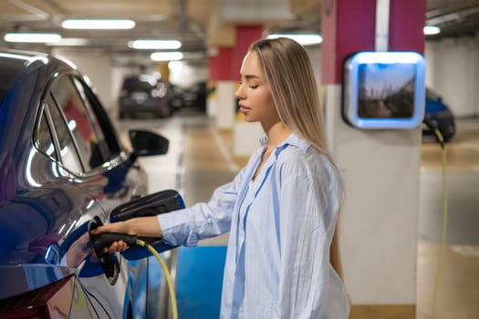 Woman charging an electric car in a parking garage, focused on energy efficiency.