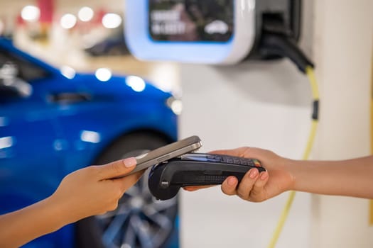Person makes a contactless payment at a terminal near a charging station with a mobile device.