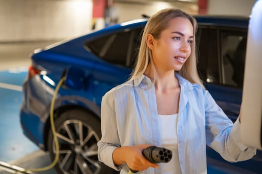 Blonde woman selects charging mode on the charging station on the parking.