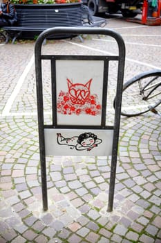 Cremona, Lombardy, Italy - November 7th 2024 Close-up of a metal sign featuring urban art depicting a cat and a lying baby, adding a touch of whimsy to a cobblestone street
