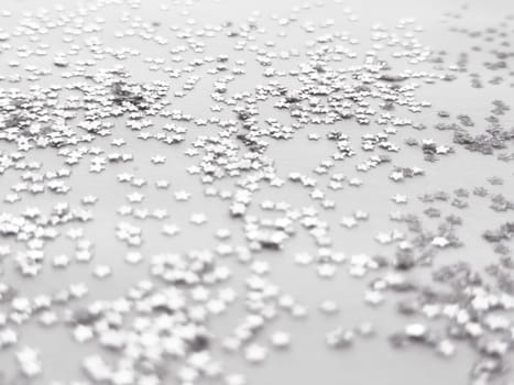 Silver metallic stars scattered on a minimalist white surface with bokeh effect.