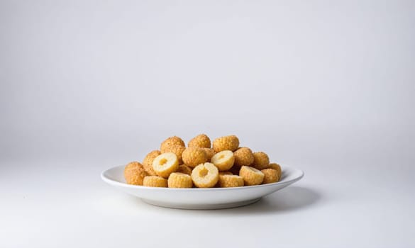 A pile of crispy, round snacks are arranged on a white plate and set against a white background. Some of the snacks are cut in half, revealing their yellow centers.
