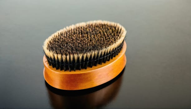 A close-up shot of a small, oval-shaped wooden brush with natural boar bristles. The brush is lying on a black surface.