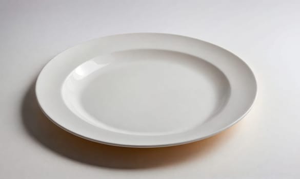 A clean, white dinner plate with a slight rim sits on a white surface. A shadow is visible beneath the plate.
