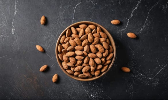 A bowl of almonds sits on a black, marbled surface. Some almonds are scattered around the bowl.