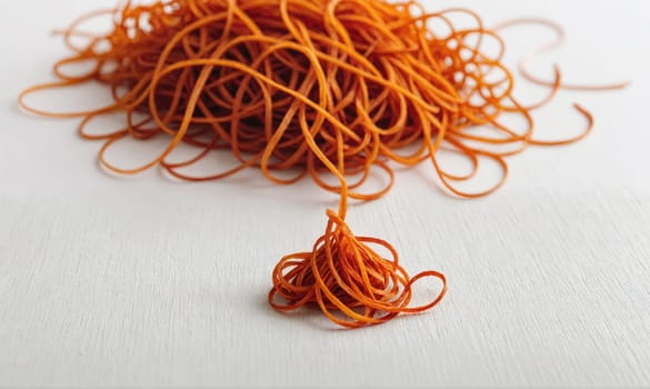 A pile of orange rubber bands is scattered on a white surface. A small pile of rubber bands sits apart from the larger pile.