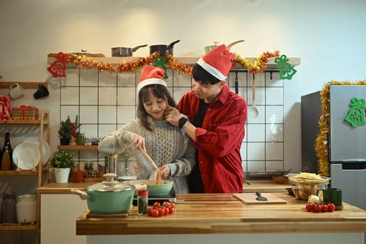 Happy young couple wearing Santa hats cooking special meal on Christmas day.