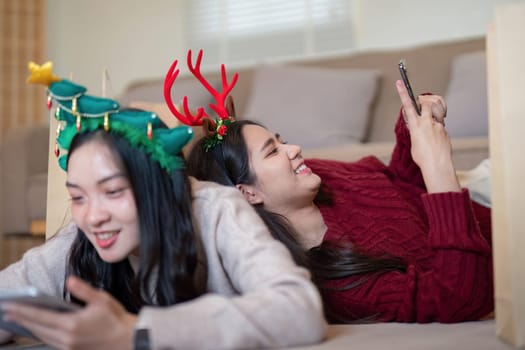 Lesbian friends wearing festive headpieces engage in joyful smartphone connection amidst Christmas decorations, celebrating inclusivity and holiday cheer.