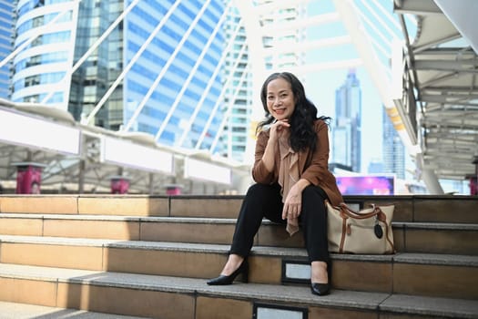 Portrait of senior businesswoman taking a break on the steps in modern cityscape.