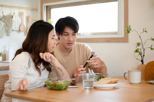 Happy young couple using smartphone during lunch in kitchen at home.