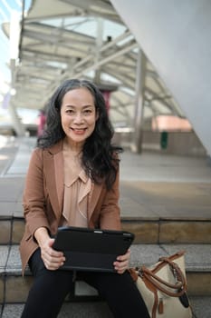 Smiling mature businesswoman working on digital tablet in urban area.
