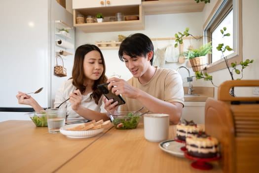 Happy young couple using smartphone during lunch in kitchen at home.