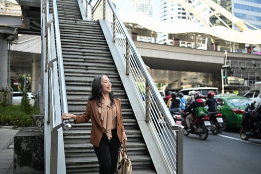 Confident senior woman walking down stairs exploring the city during daytime.