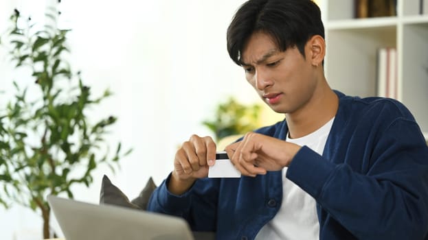 Young asian man destroying his credit card in frustration. Financial management and debt reduction concept.