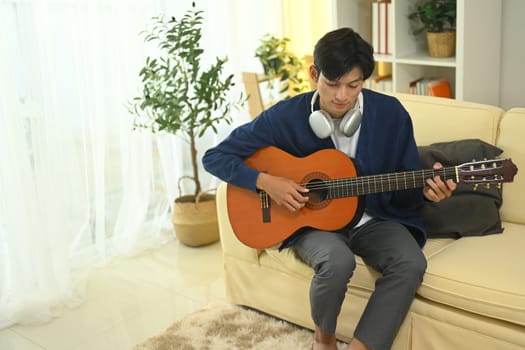Young man relaxing on sofa and playing guitar in natural light.