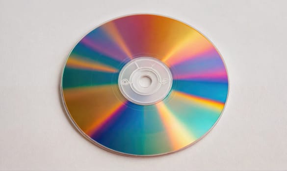 A CD with a rainbow effect on its surface lies on a plain white background. The CD's center is a clear plastic hub with a small opening.