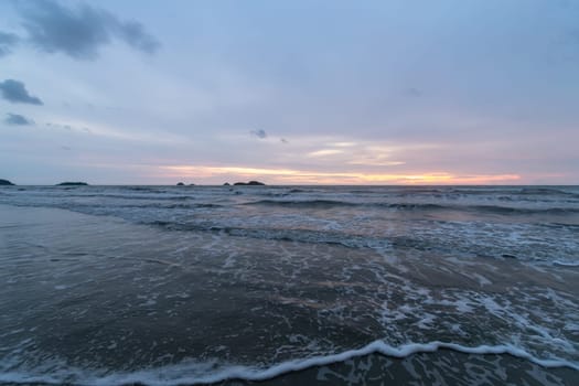 A serene coastal scene shows gentle waves on the shore and a stunning sunset reflecting on the waters surface