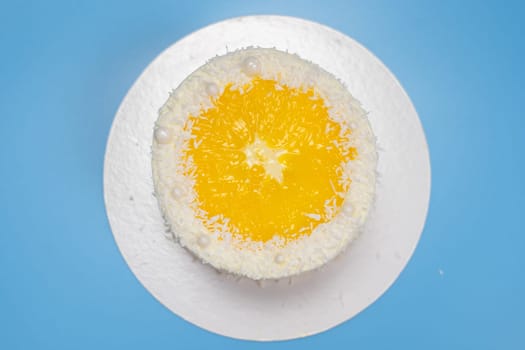 Delicious round yellow cake with orange slice and coconut flakes on blue background, top view