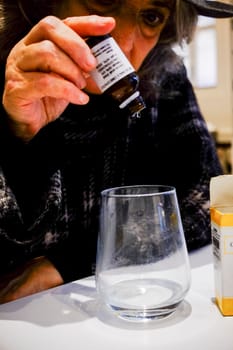 Cremona, Lombardy, Italy - November 7th 2024 Senior woman carefully pouring cbd oil drops from a dropper bottle into a glass of water, preparing her daily dose of cannabidiol