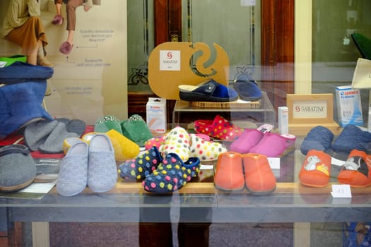 Cremona, Lombardy, Italy - November 7th 2024 Various slippers are neatly arranged in a store window display, showcasing different colors, patterns, and materials for sale