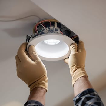 Hands wearing gloves install an LED ceiling light, focusing on the intricate wiring and secure attachment.