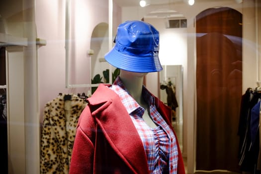 Cremona, Lombardy, Italy - November 7th 2024 Stylish mannequin showcasing a red coat and blue bucket hat in a clothing store window, promoting the latest fashion trends