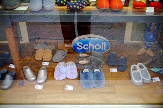 Cremona, Lombardy, Italy - November 7th 2024 Colorful and comfortable slippers are displayed for sale in a shoe store window, featuring a prominent scholl sign