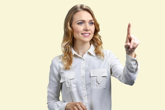 Smiling blond woman is touching transparent virtual screen. Pastel yellow background.