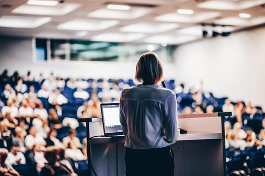 Female speaker giving a talk on corporate business conference. Unrecognizable people in audience at conference hall. Business and Entrepreneurship event