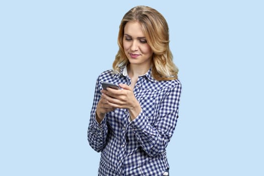 Portrait of woman typing something on smartphone. Isolated on pastel blue background.