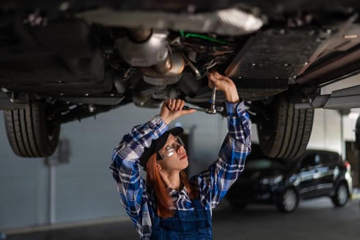 Female mechanic unscrew the nuts on the bottom of the car that is on the lift. A girl at a man's work