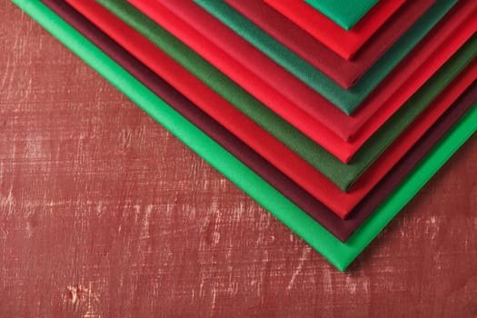Stack of red and green fabrics on brown background, space for text