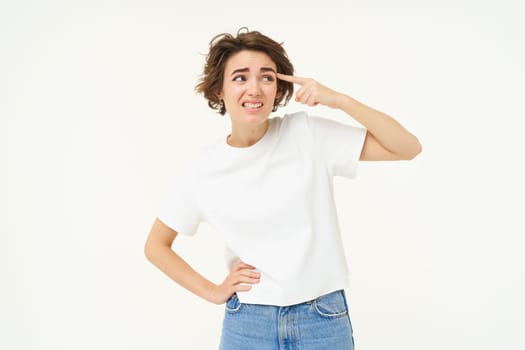 Portrait of woman complaining at someone, pointing finger at forehead, standing over white background.
